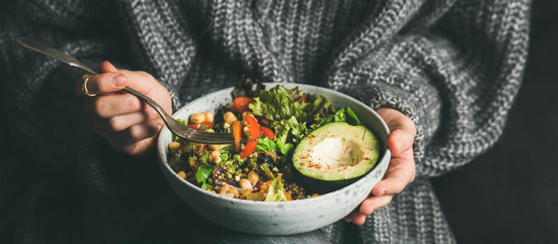 Woman holds bowl with avocado and salad