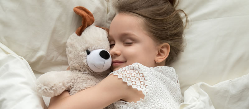 Young girl hugs teddy bear in white bed