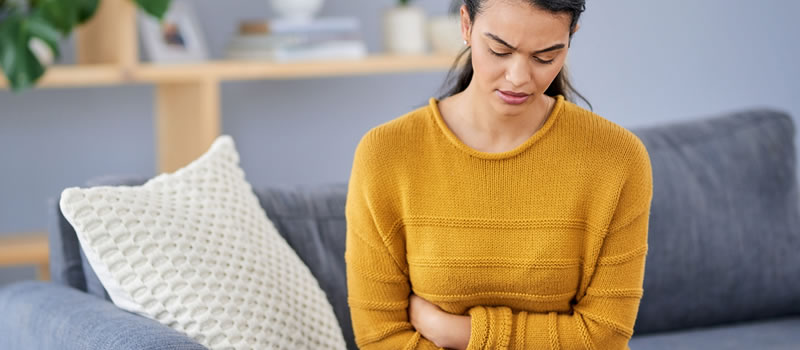 Woman sitting on couch holds her stomach in pain