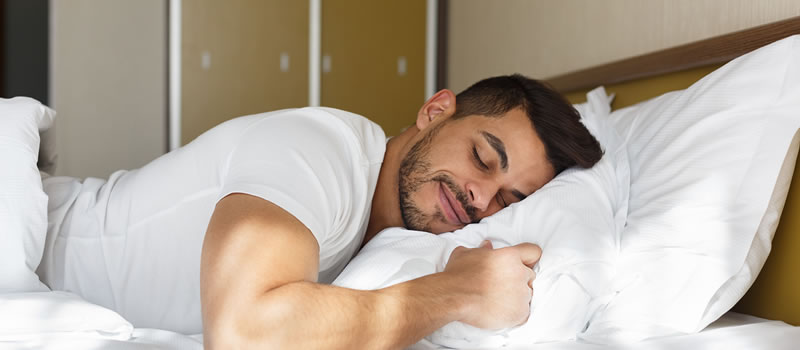 Man in white shirt sleeps happily on white pillows